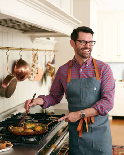 John Kanell cooking vegetables in a skillet on a gas range
